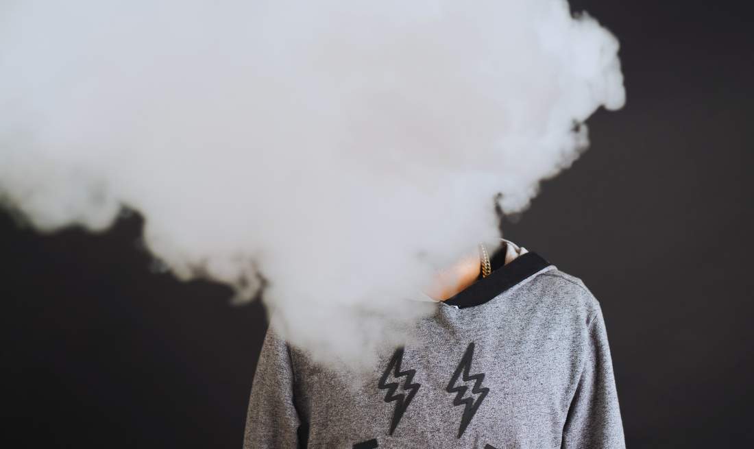 une personne qui vapote avec plein de fumée devant sa tête