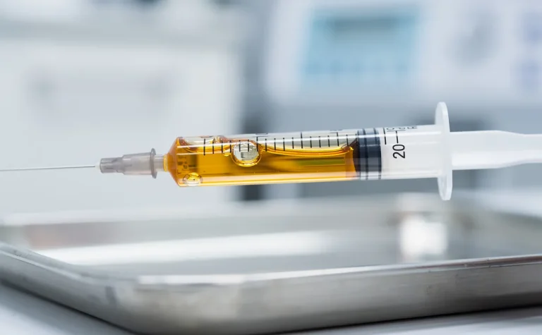 Une seringue remplie de plasma doré est tenue au-dessus d’un plateau médical dans une clinique claire et stérile.