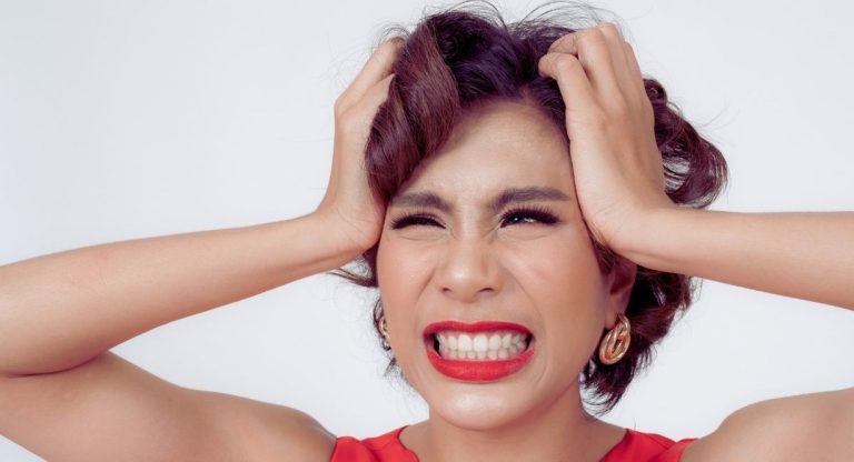 Femme serrant fortement les dents et se tenant la tete, signe de stress et de bruxisme