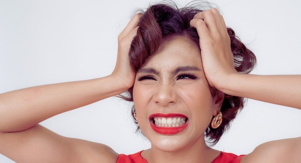 Femme serrant fortement les dents et se tenant la tete, signe de stress et de bruxisme