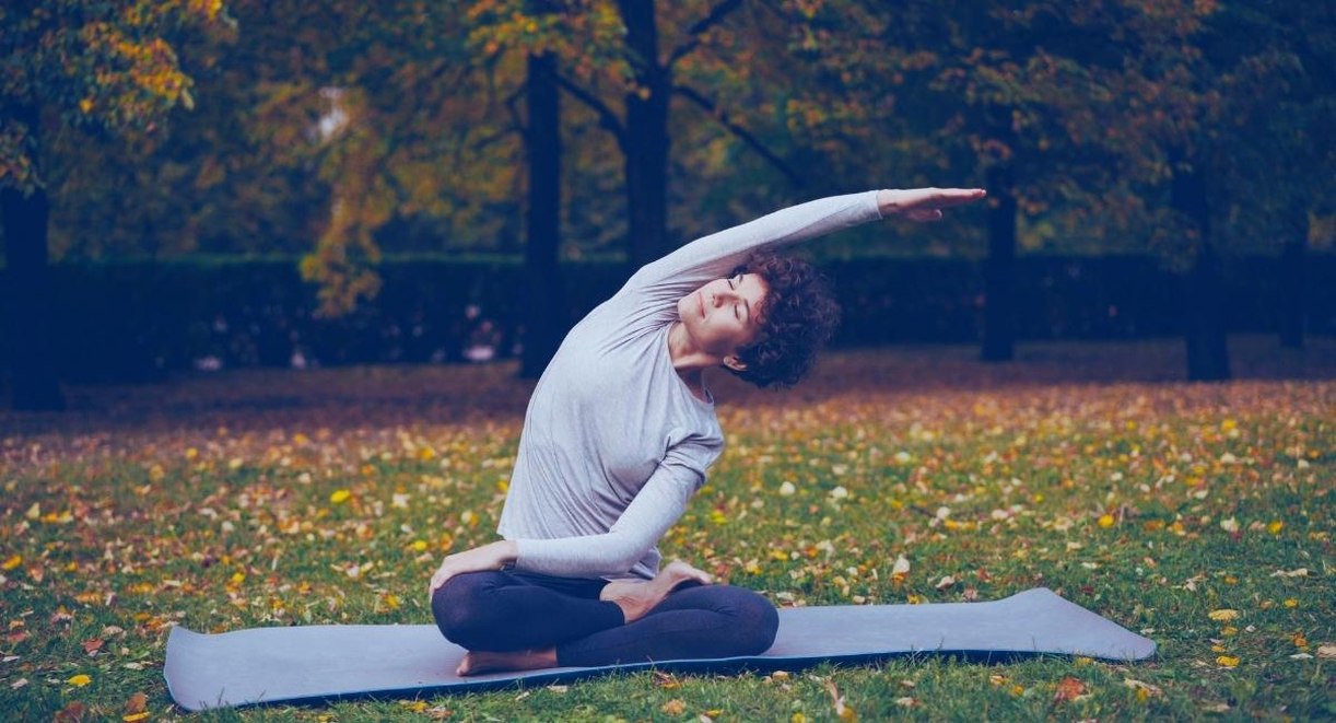 Femme assise en tailleur sur un tapis, realisant un etirement lateral dans un parc aux feuilles d automne